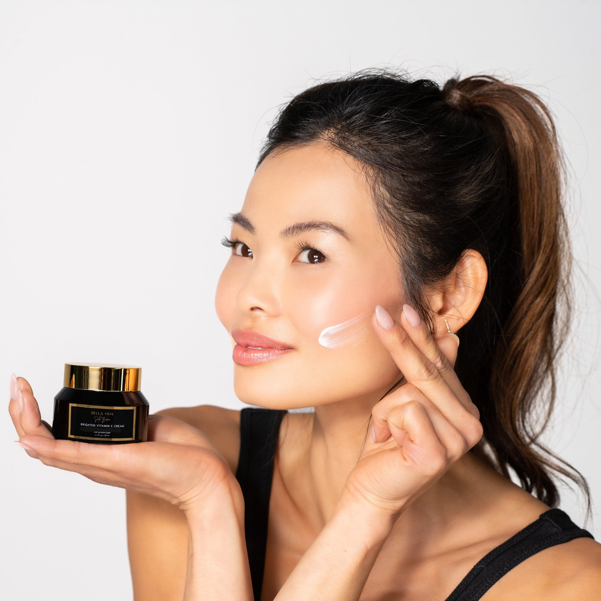 Woman applying cream to face with A jar of Bella Vida Santa Barbara Brighten Vitamin C Cream with two Beauty Shortlist 2025 and 2024 Award Winner 